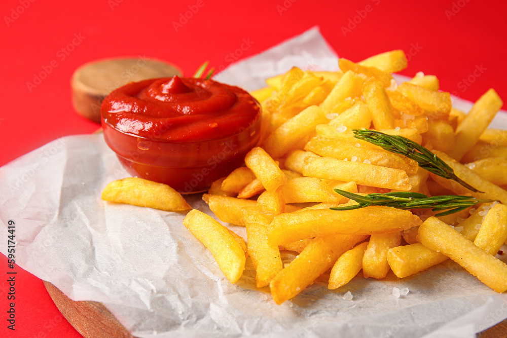 Wooden board with tasty french fries and ketchup on red background, closeup