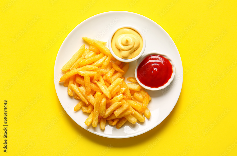 Plate with tasty french fries and sauces on yellow background