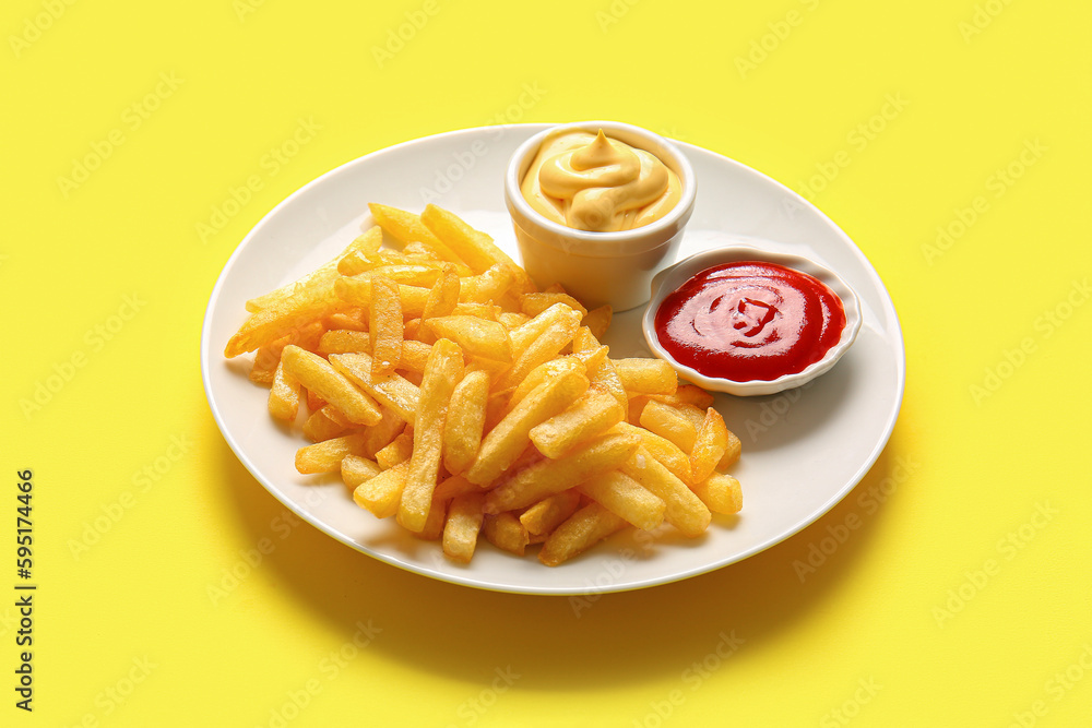 Plate with tasty french fries and sauces on yellow background