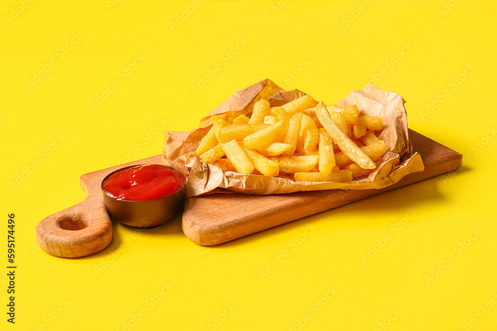 Wooden board with tasty french fries and ketchup on yellow background