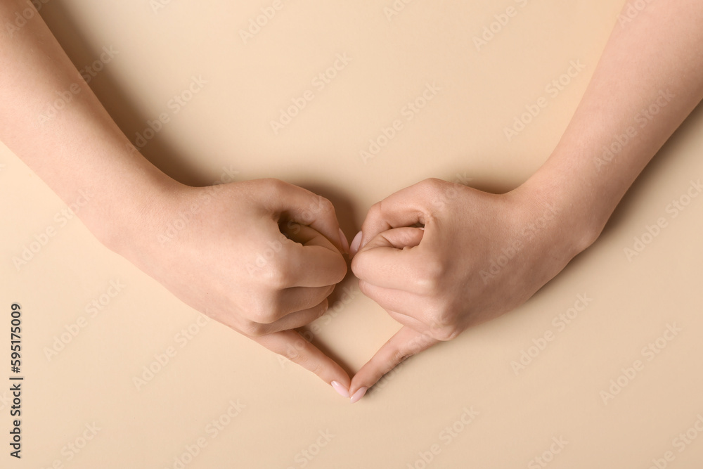 Woman making heart with her hands on beige background