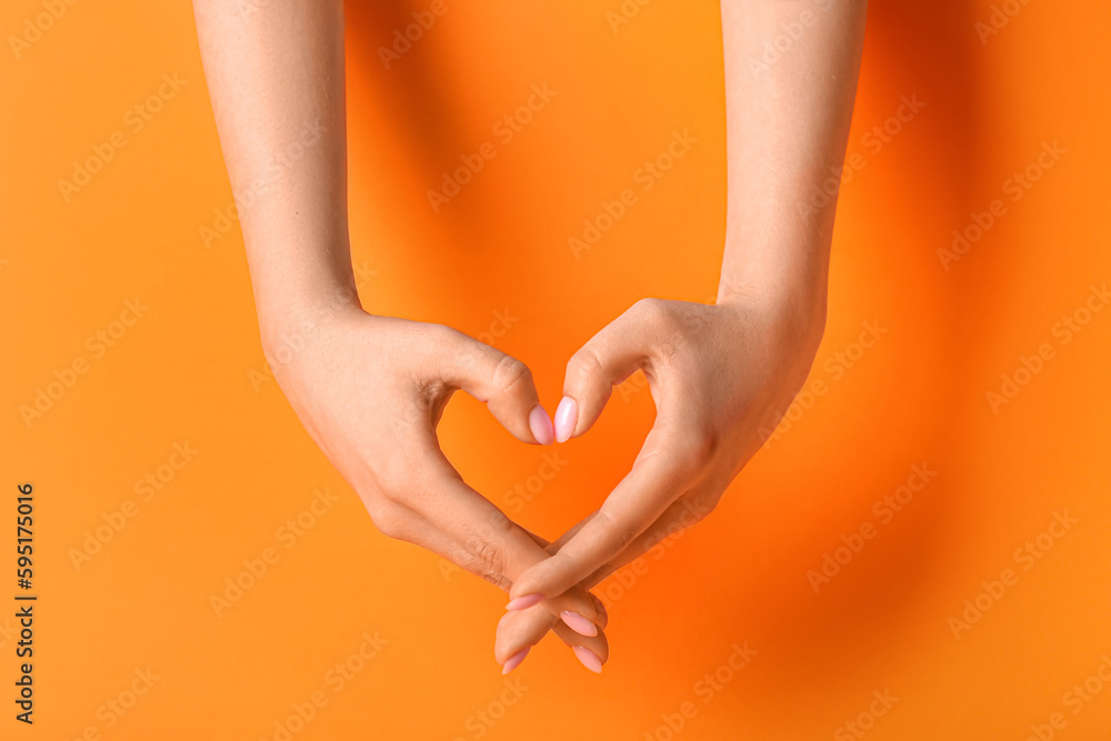 Woman making heart with her hands on orange background