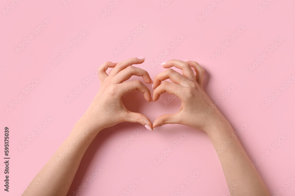 Woman making heart with her hands on pink background