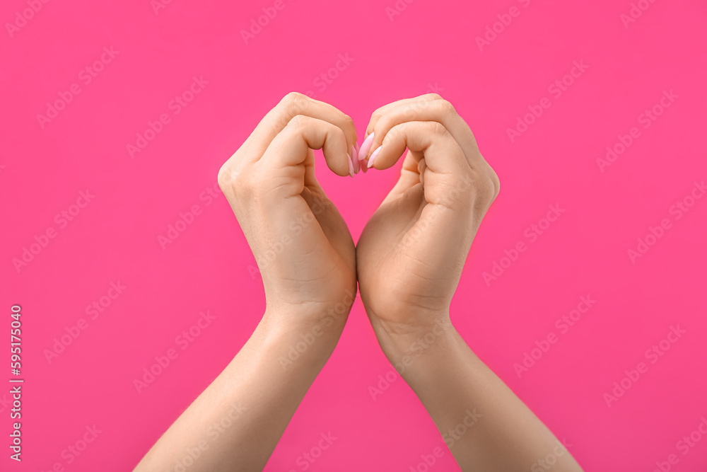 Woman making heart with her hands on pink background