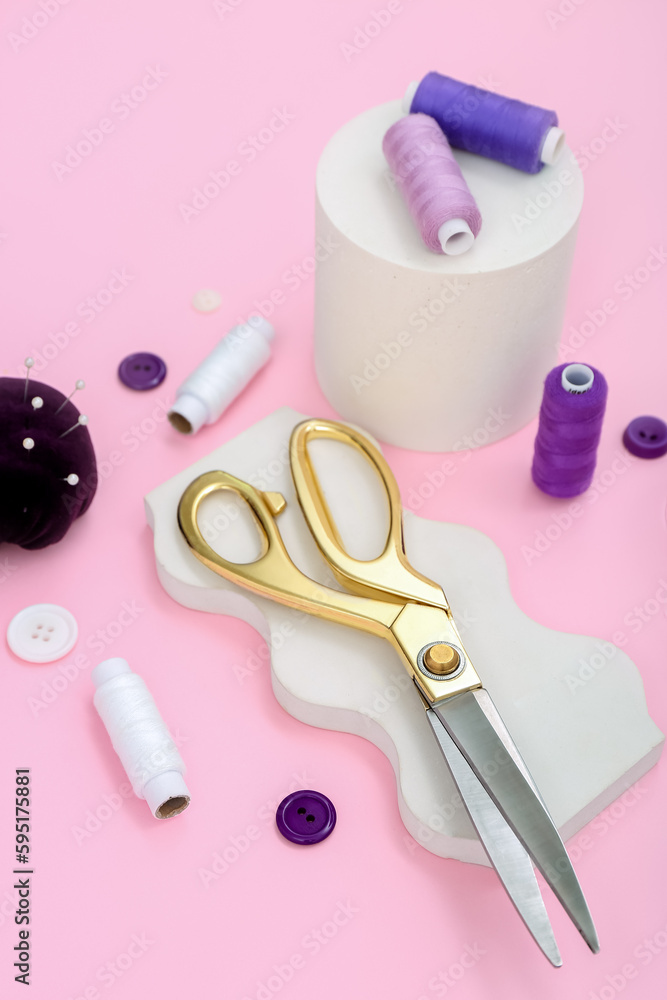 Podiums with scissors, buttons and thread spools on pink background