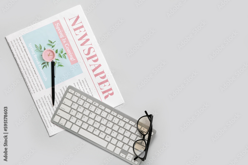 Newspaper with pen, computer keyboard and eyeglasses on light background