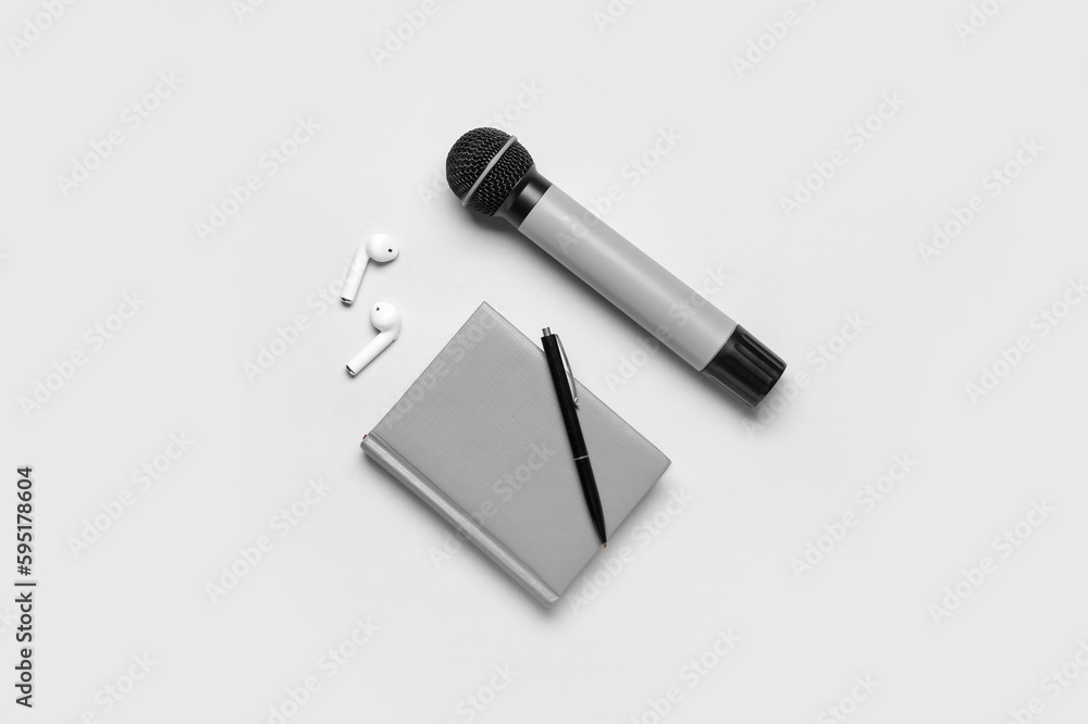 Notebook with pen, microphone and earphones on light background