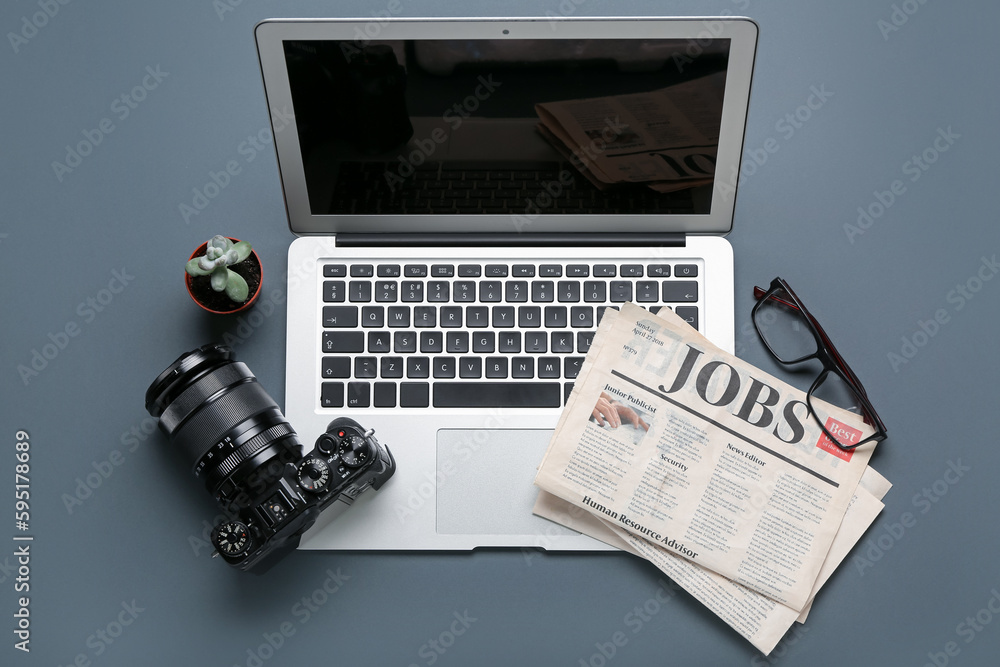 Laptop with newspapers, eyeglasses and photo camera on dark background