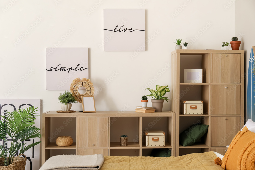 Interior of light bedroom with houseplants and shelving unit