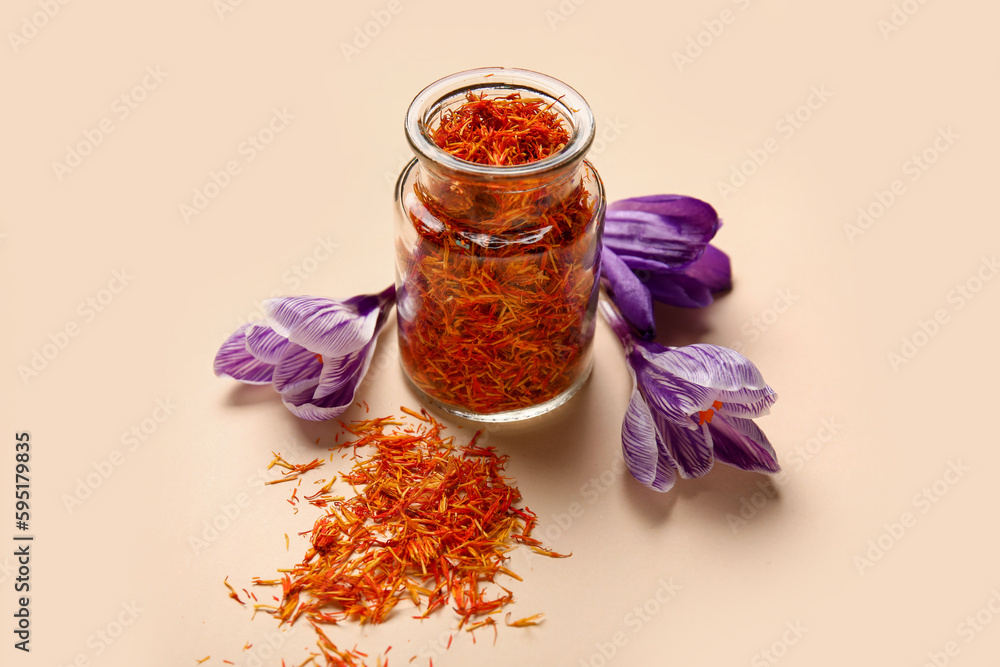 Jar of dried saffron threads and crocus flowers on beige background