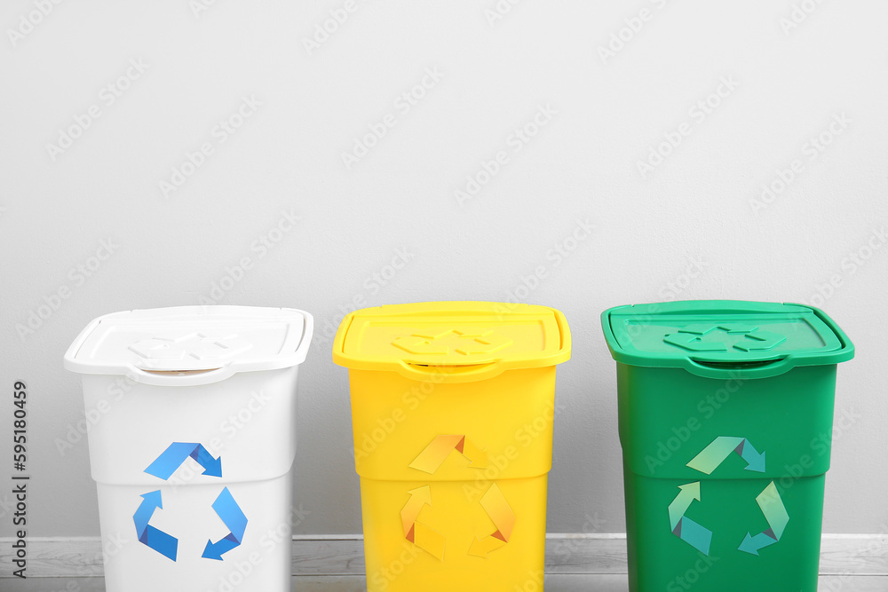 Different garbage bins with recycling symbol near white wall