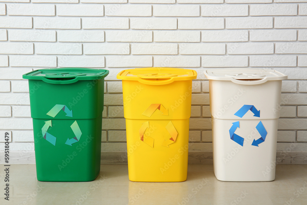 Different garbage bins with recycling symbol near white brick wall