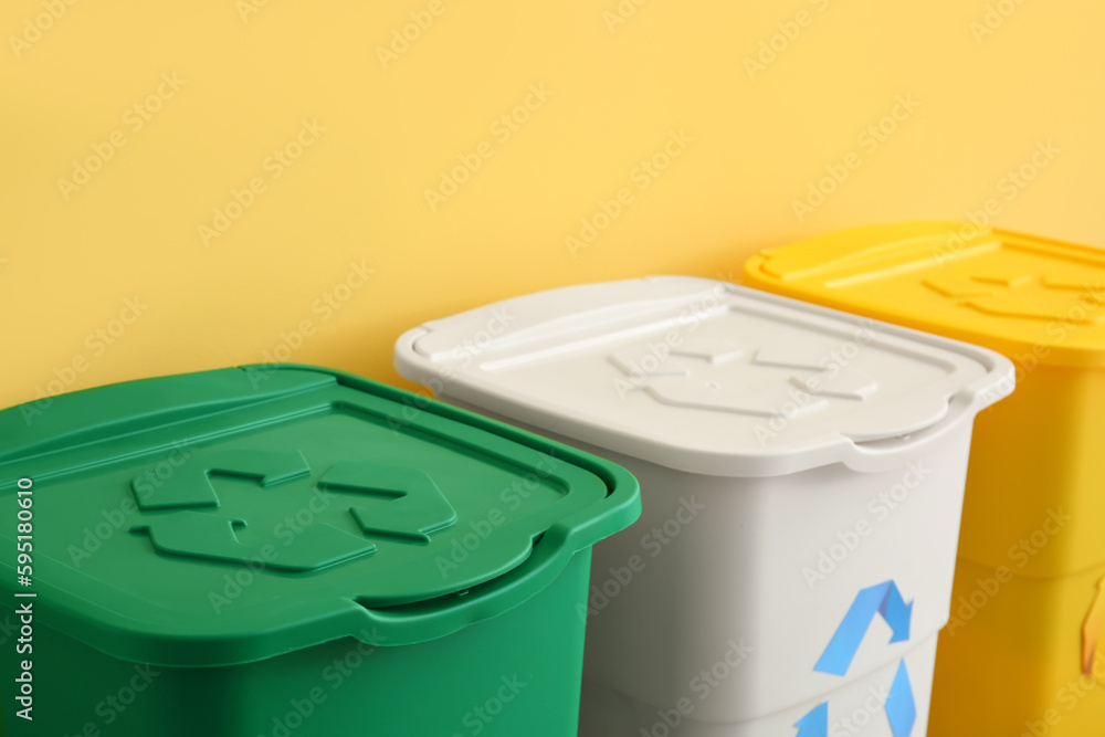 Different garbage bins with recycling symbol near yellow wall