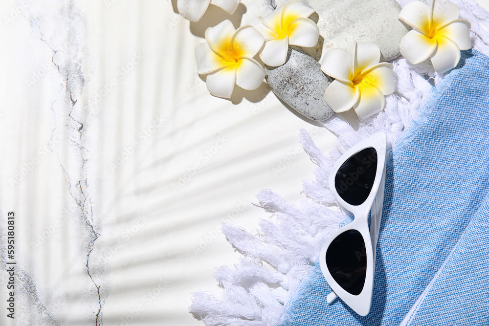 Composition with sunglasses, towel and plumeria flowers on white marble background