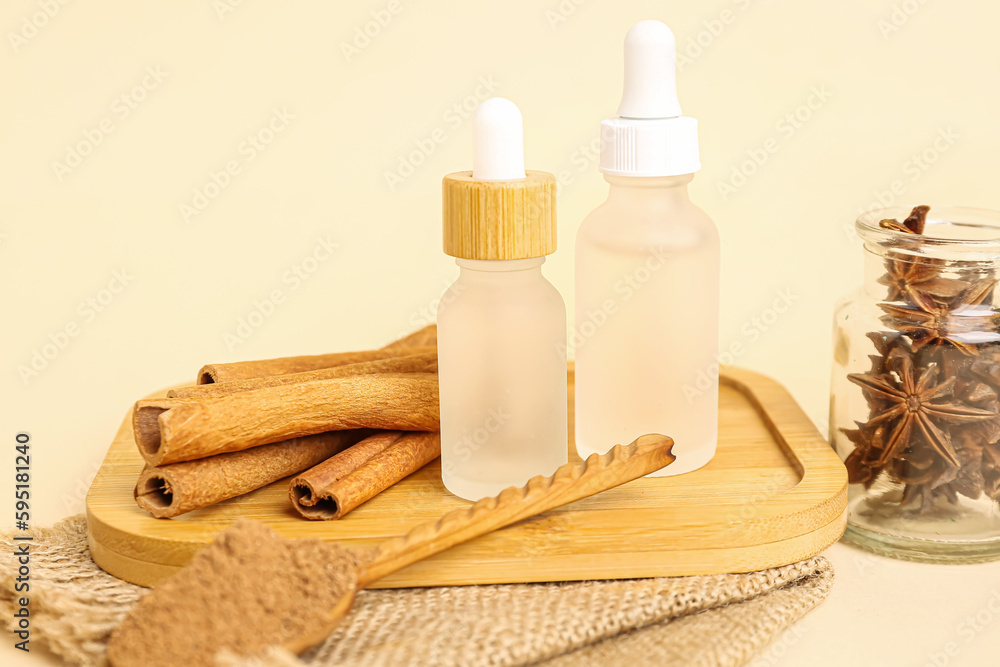 Board with bottles of essential oil, cinnamon sticks, powder and anise on beige background