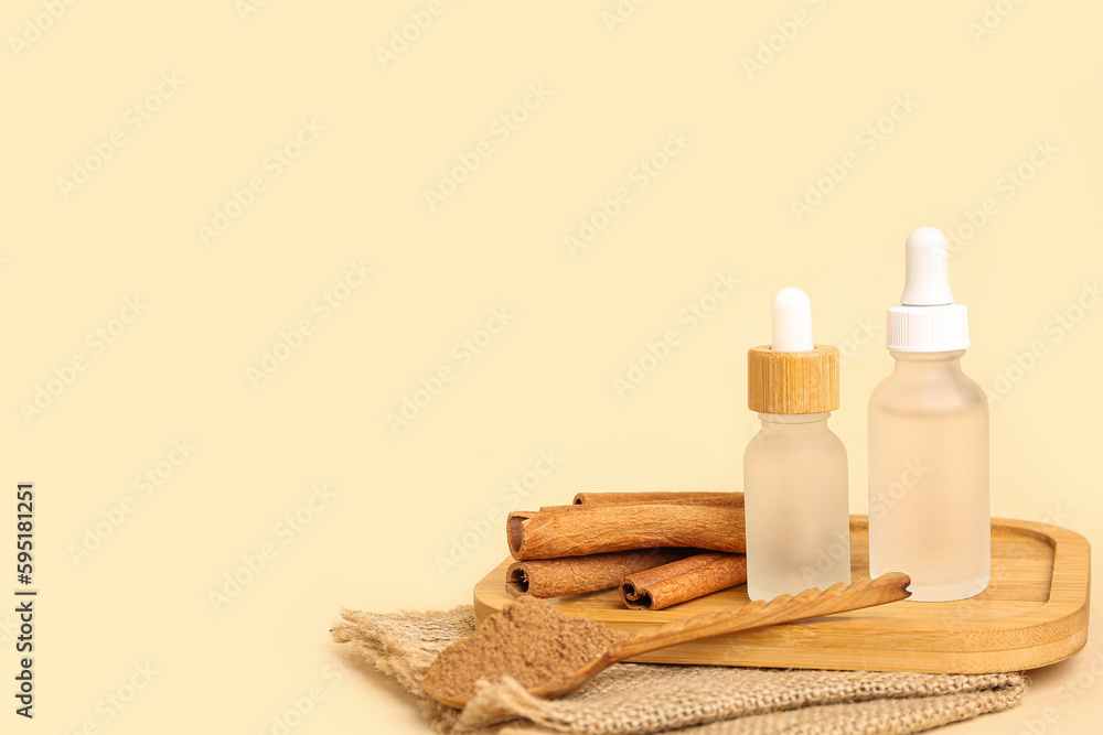 Board with bottles of essential oil, cinnamon sticks and powder on beige background