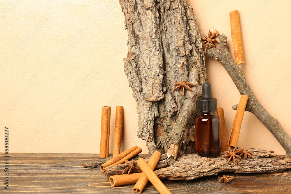 Bottle of essential oil with cinnamon sticks, anise and tree barks on table near beige wall