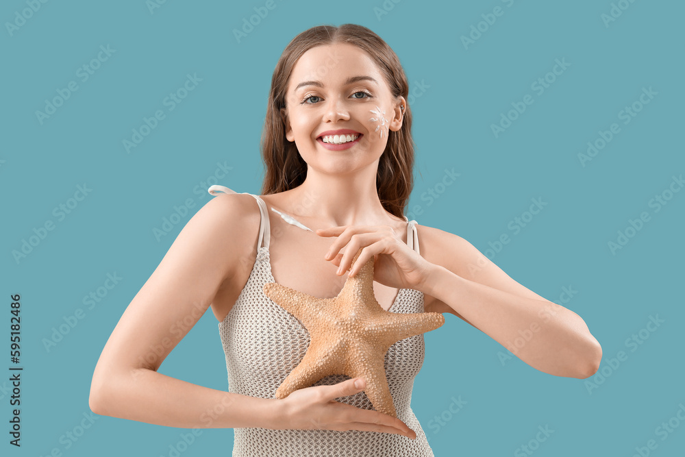 Beautiful young woman with sunscreen cream on her face and starfish on blue background