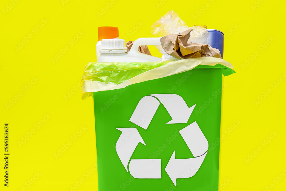 Trash bin with different garbage on yellow background