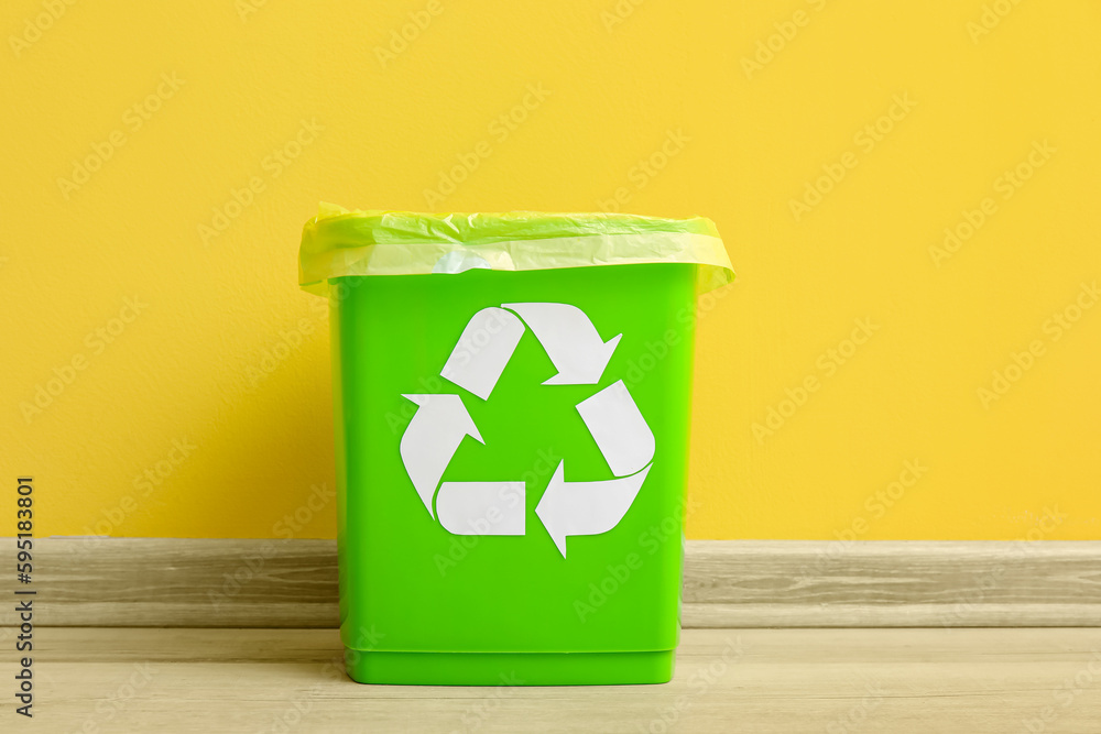 Trash bin with recycling symbol near yellow wall