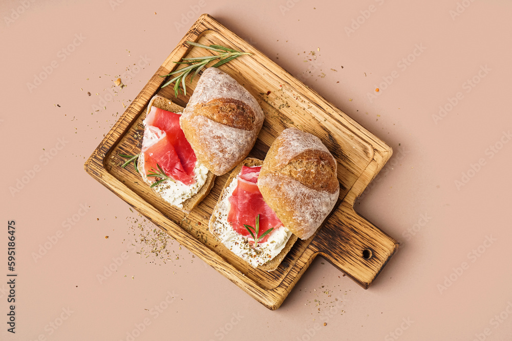 Wooden board of tasty sandwiches with jamon on beige background