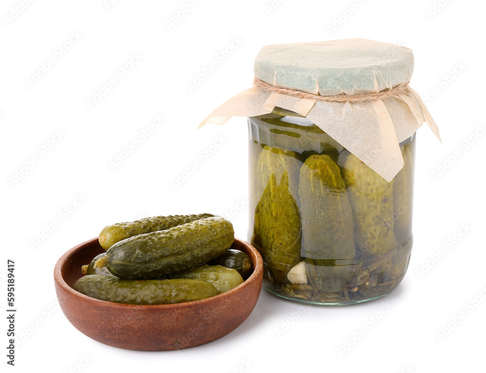 Jar and bowl with tasty fermented cucumbers on white background