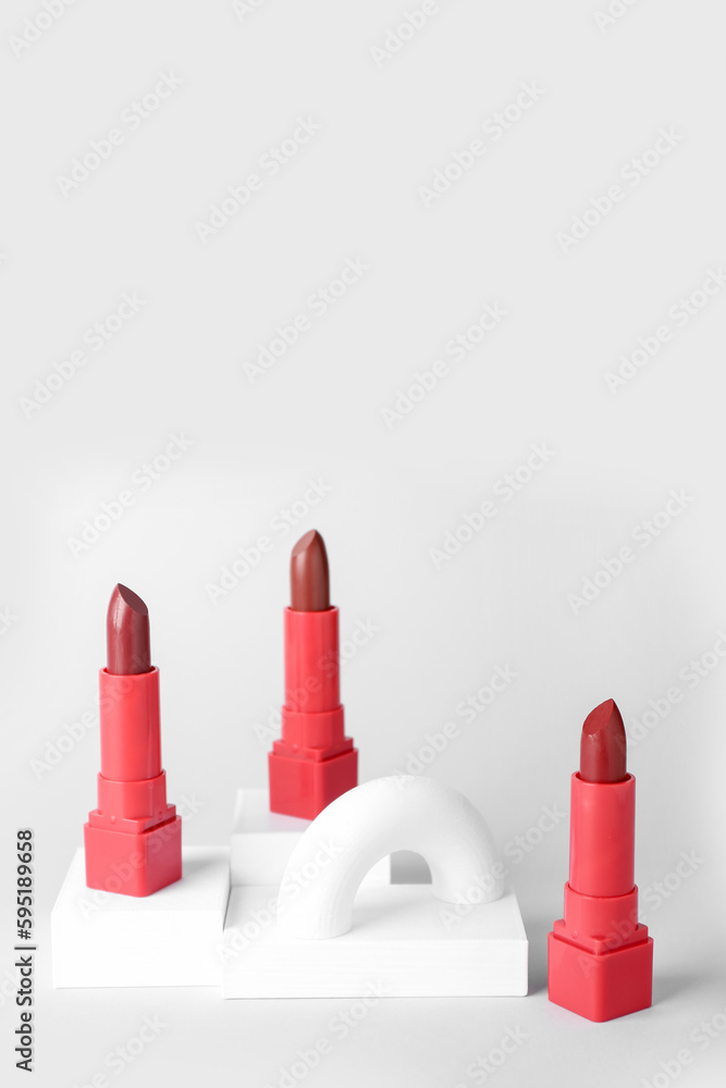 Decorative plaster podiums and lipsticks on grey background