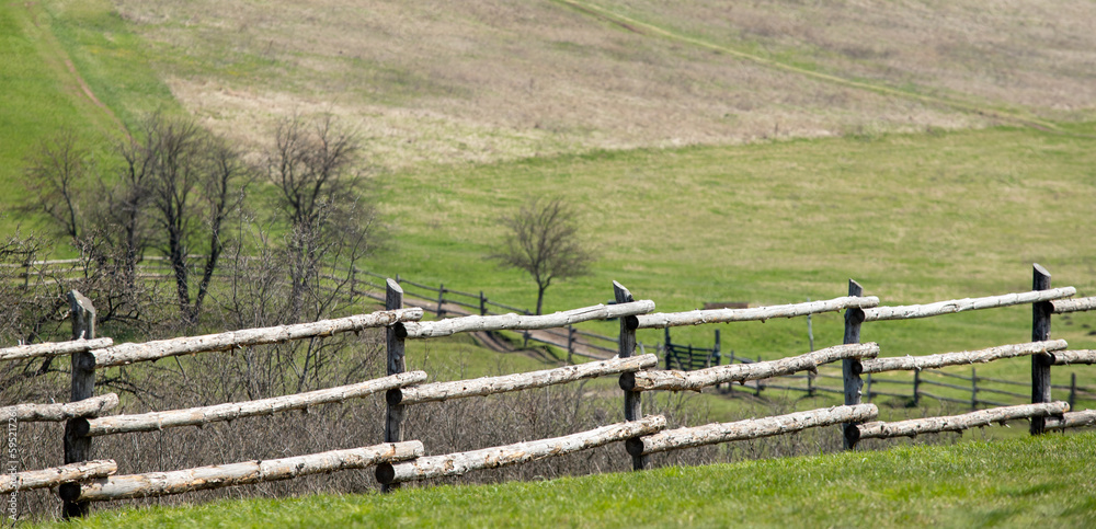 log fence along a green field against the sky