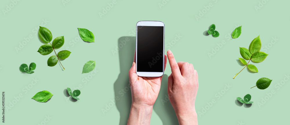 Person using a smartphone with green leaves - flat lay