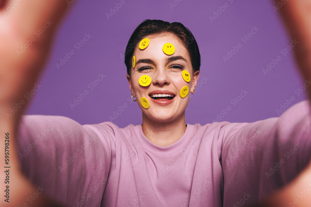 Playful young woman taking a selfie with smiley stickers on her face