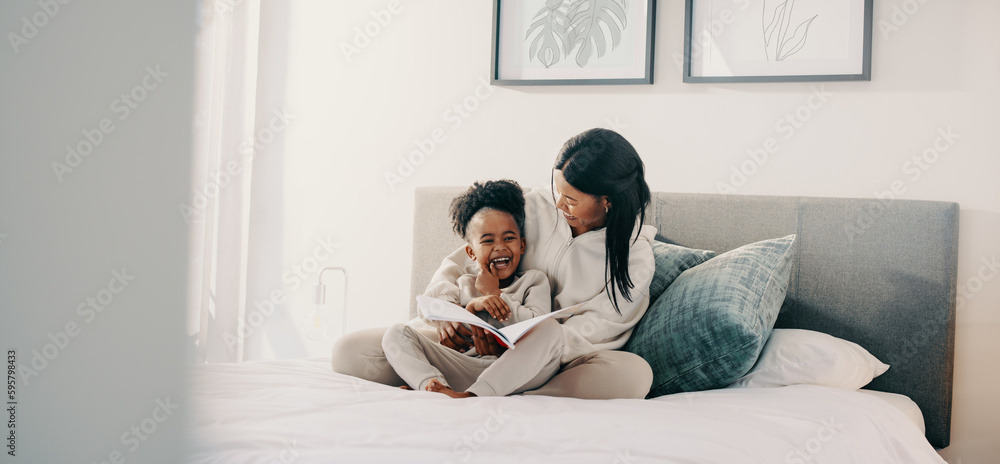 Mom and daughter laughing together as they read a story book on a bed