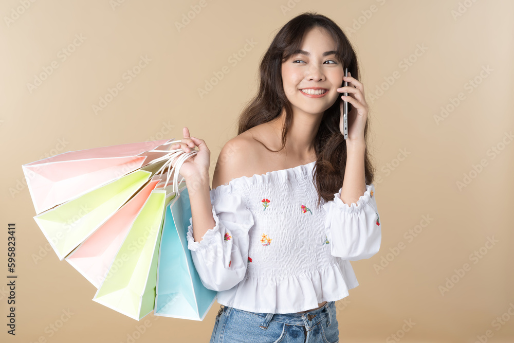 Young Asian woman usin shopping bag using phone on isolate brown background