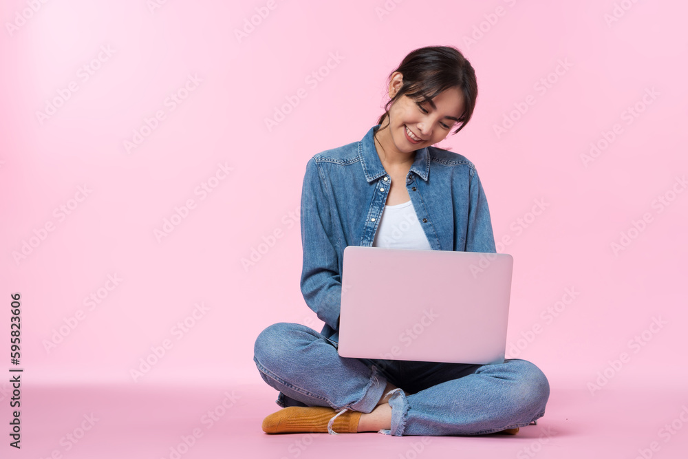 Young Asian college student sits cross-legged on floor working with a laptop computer, looking at th