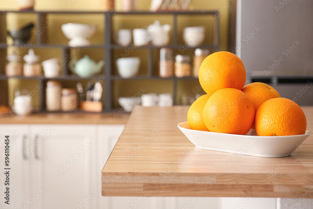 Plate with oranges on table in stylish kitchen