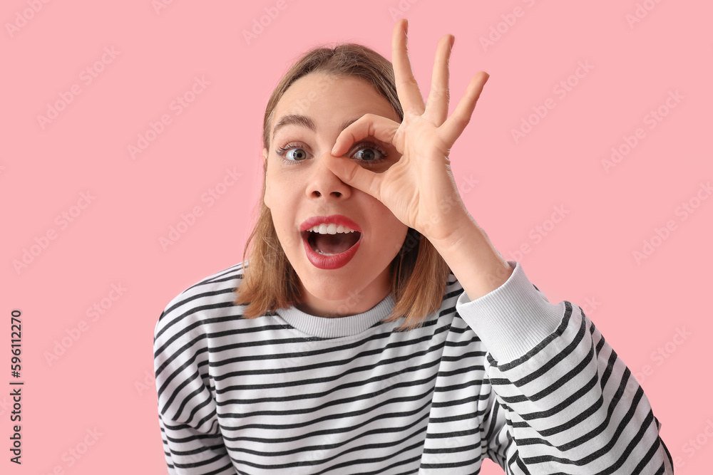 Funny young woman in striped sweatshirt showing OK on pink background, closeup