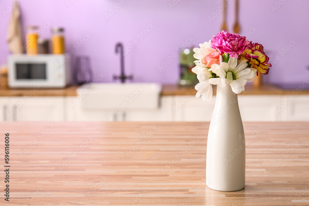 Vase with beautiful flowers on wooden table in kitchen