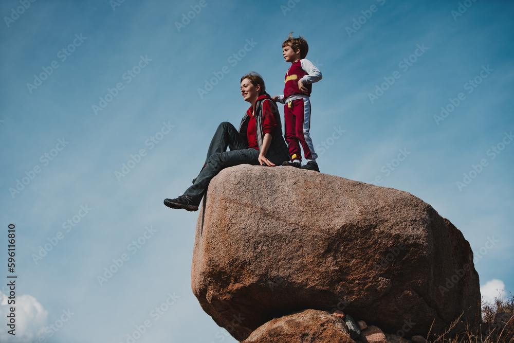 Mother and son sits on a big boulder and admiring the scenery