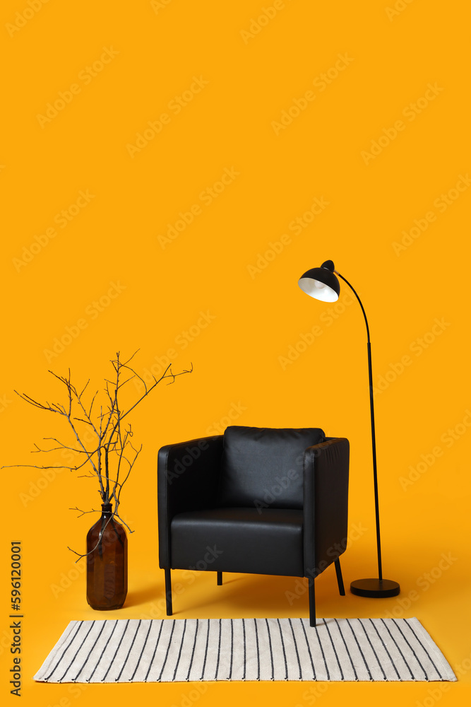 Modern black armchair, lamp and vase with branches on orange background