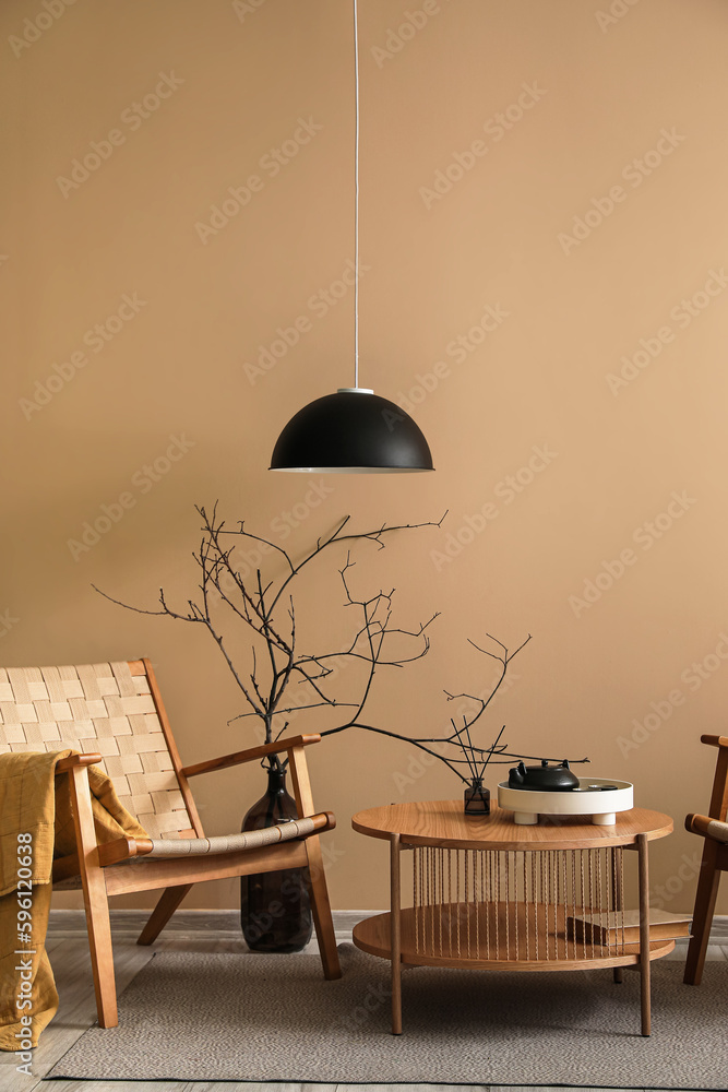 Cozy armchair, coffee table and vase with branches near beige wall