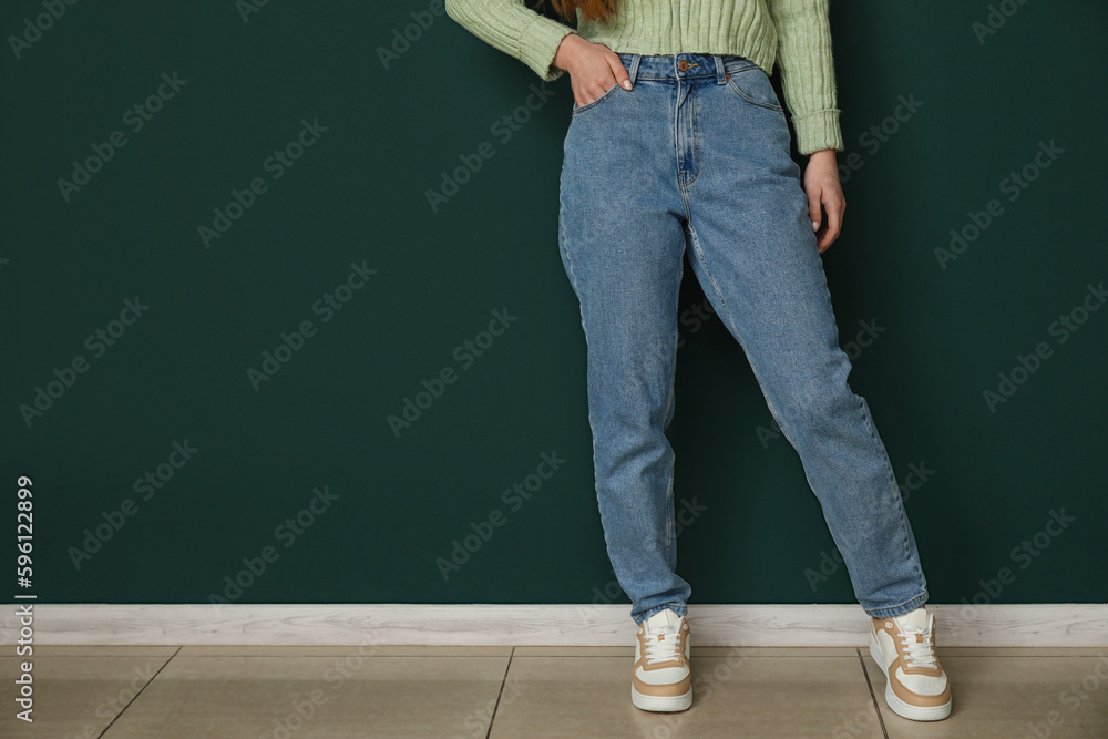 Young woman in stylish jeans near green wall