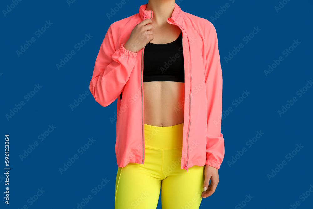 Sporty young woman in jacket on blue background