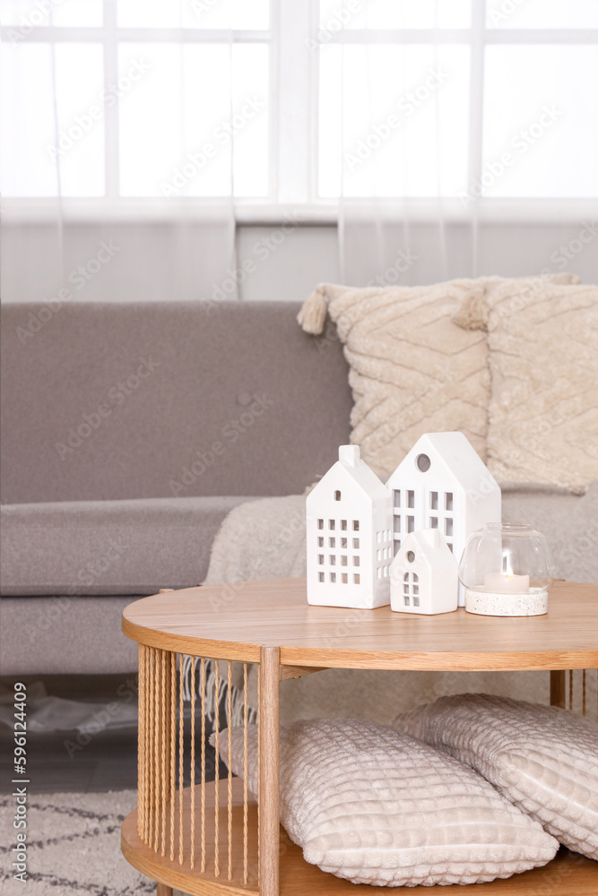 Coffee table with decorative houses and burning candle in interior of living room