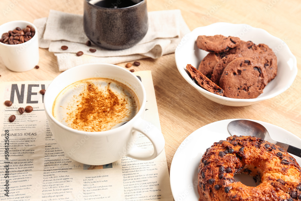 Cup of coffee with newspaper and pastry on light wooden table, closeup