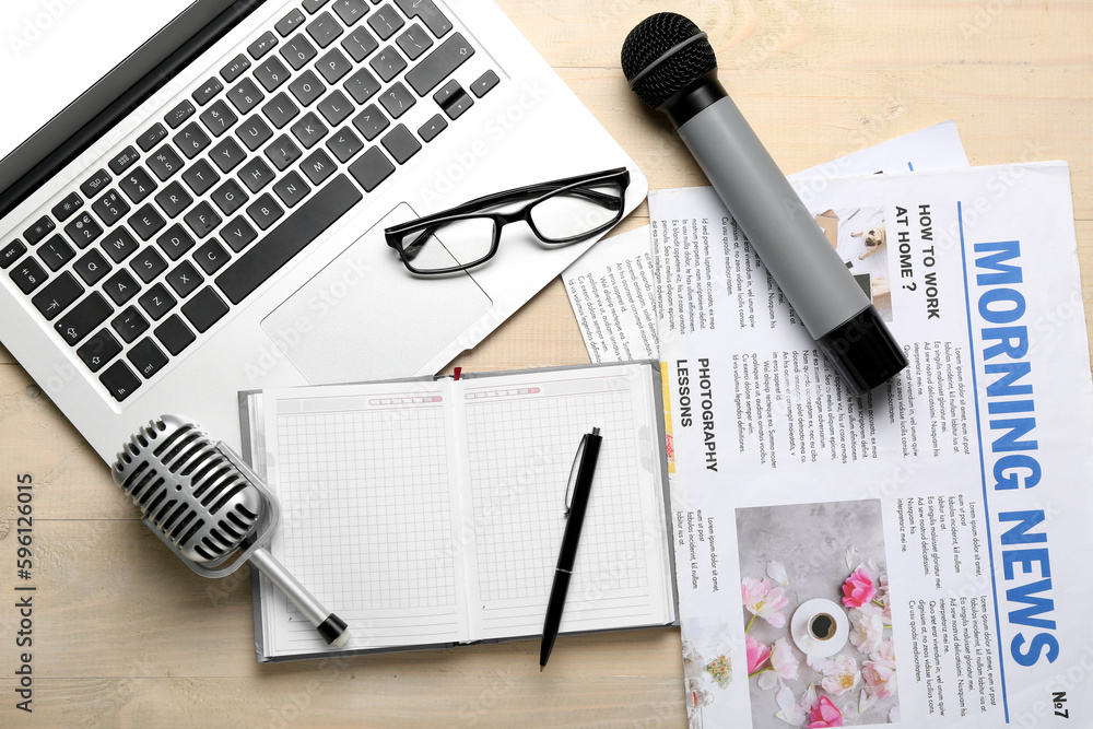 Laptop with eyeglasses, microphones, notebook and newspapers on light wooden background