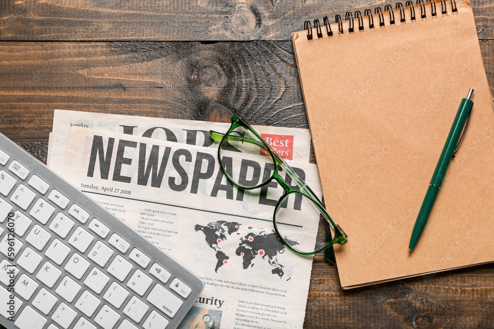 Newspaper with eyeglasses, computer keyboard and notebook on dark wooden background