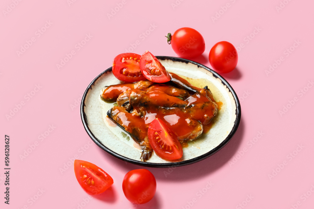 Plate with canned fish in sauce and tomatoes on pink background