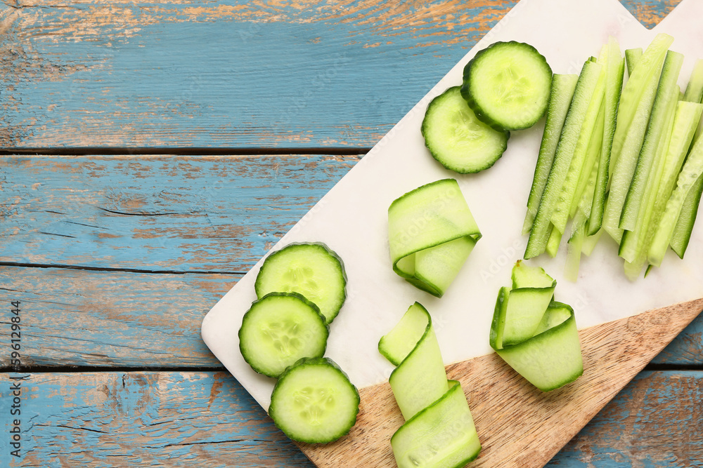 Board with fresh cut cucumber on blue wooden background