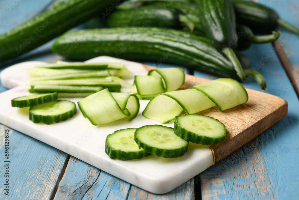 Board with fresh cut cucumber on blue wooden background, closeup