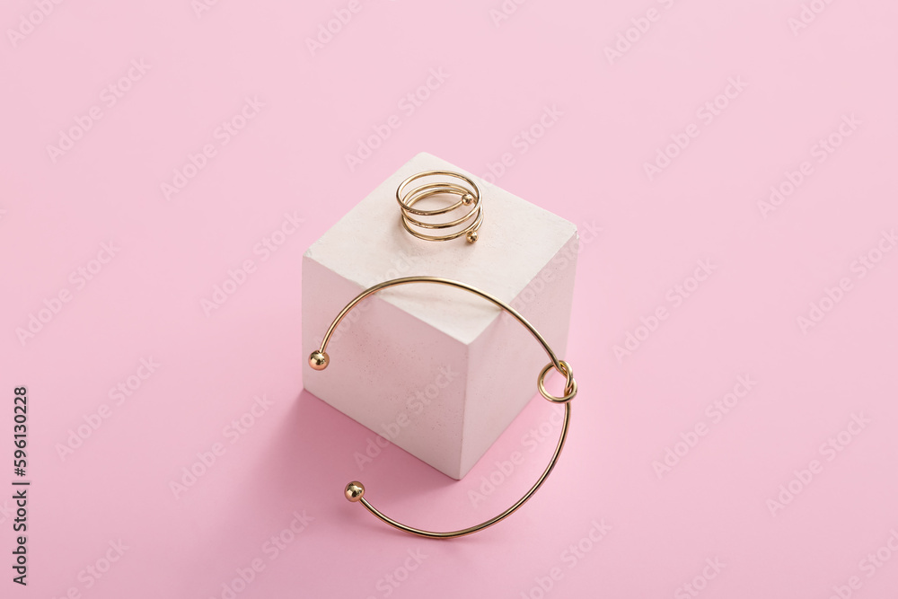 Showcase pedestal with golden ring and bracelet on pink background