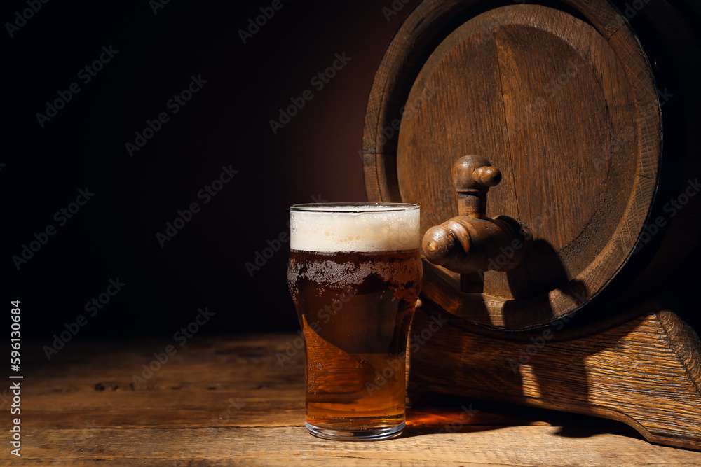 Wooden barrel and glass of cold beer on table against dark background